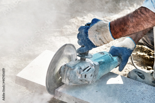 Hands of a pavement construction worker using an angle grinder for cutting the tiles