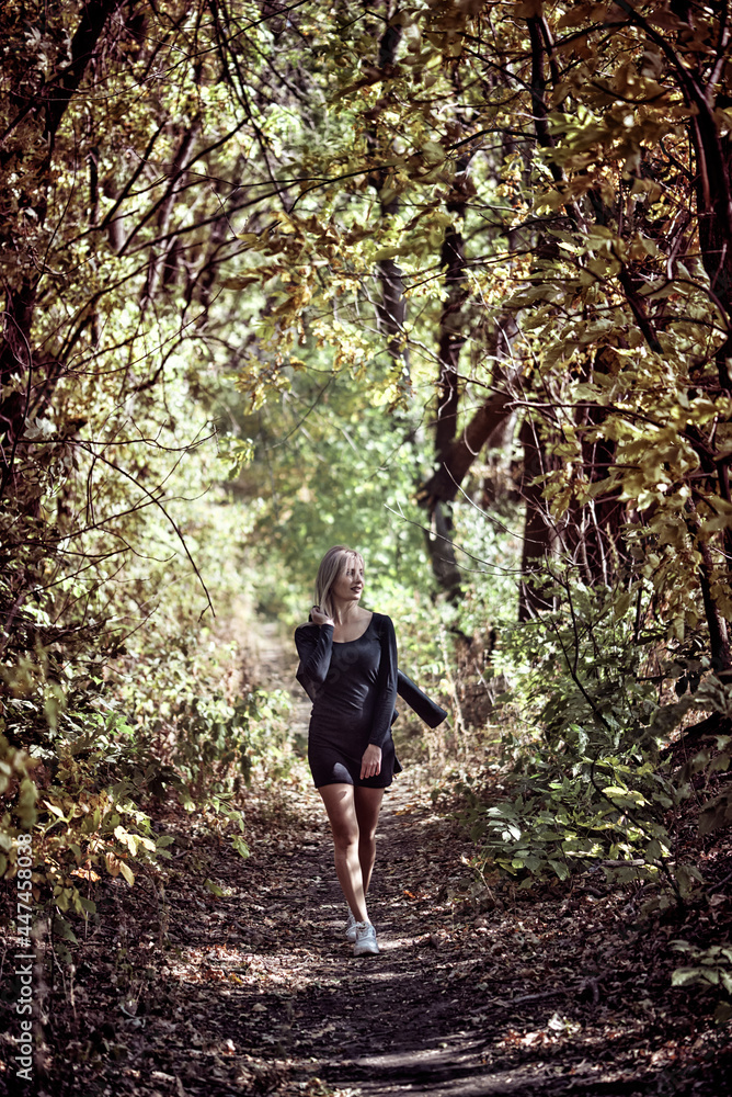Sexy Young woman in a little black dress and biker jacket walking In Forest During Autumn.