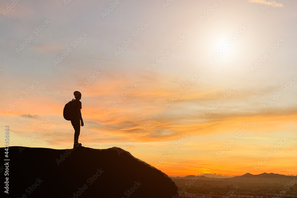 Silhouette of young traveler and backpacker standing and watched beautiful view sunset alone on top of the mountain. He enjoyed traveling and was successful when he reached the summit.