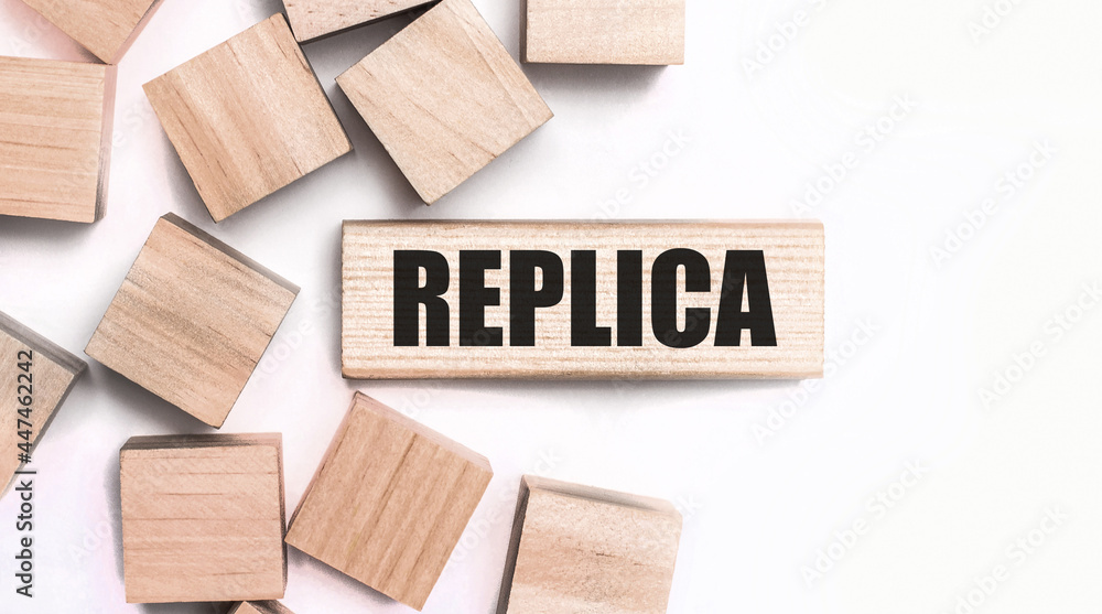 On a light background, wooden cubes and a wooden block with the text REPLICA. View from above On a light background, wooden cubes and a wooden block with the text REPLICA. View from above