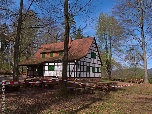 Closed restaurant in historic half-timbered building surrounded by trees in spring season near Annweiler am Trifels, Germany in Palatinate Forest. Outdoor seating shut with barrier tape. © Timon