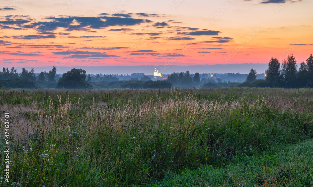 Obraz premium Colorful sunrise in rural with bright sky in the background colored by rising sun. A church and trees look out from a foggy meadow. Dusk and dawn, agriculture, travel, tourism, scenic views, hiking.