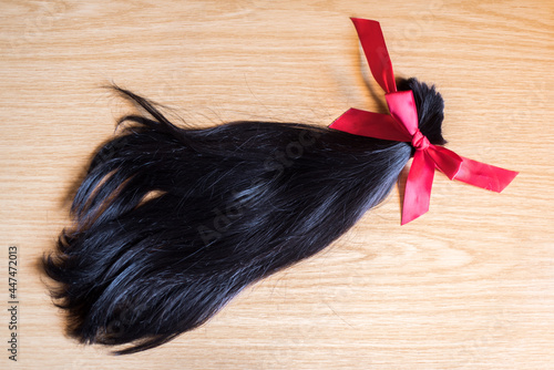 Mechón de pelo cortado anudado con un lazo de raso rojo sobre un fondo de madera. Donación de cabello para pelucas para pacientes con cáncer photo