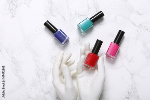 Mannequin hand holds bottles of nail polish on marble background. Beauty layout