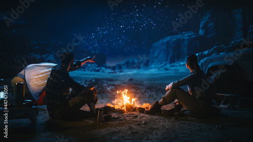 Lovely Young Couple Sitting by Campfire Watching Night Sky while Camping in the Canyon. Girlfriend and Boyfriend Tell Inspirational Nature Loving Stories about Life, Look at Milky Way Stars