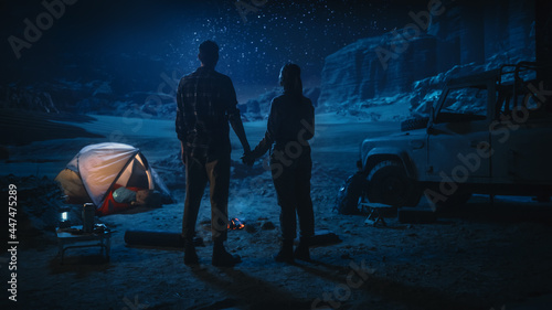 Happy Couple Camping in the Canyon at Night, Standing by Campfire, Holding Hands Lovingly and Romantically Watching Star Sky. Two Traveling people on a Nature Inspirational Vacation Trip, Journey 