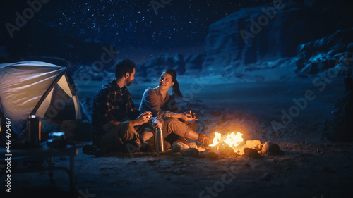 Happy Couple Nature Camping in the Canyon, Sitting by Campfire, Drinking Coffee, Watching Night Sky. Two Traveling Young people Talk, Look at Milky Way Stars. On Inspirational Vacation Trip