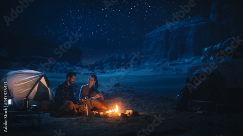 Happy Couple Nature Camping in the Canyon, Sitting Watching Campfire Together, Talking, Watching Night Sky. Two Traveling Young people On Inspirational Vacation Trip Marvel at Milky Way Stars