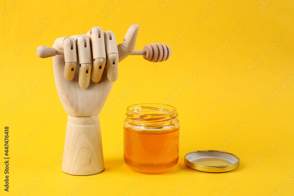 Bee honey jar and wooden hand holding honey wooden spoon on yellow background