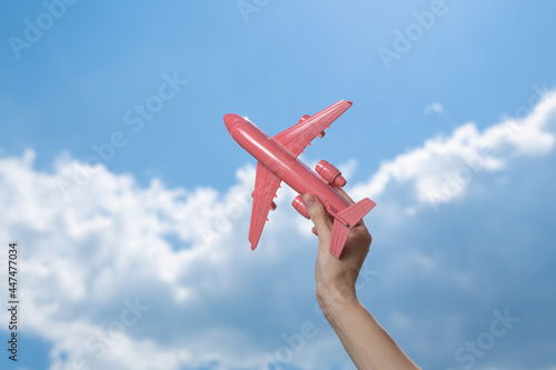 Hand holds pink model airplane on background of blue sky with clouds. Travel concept