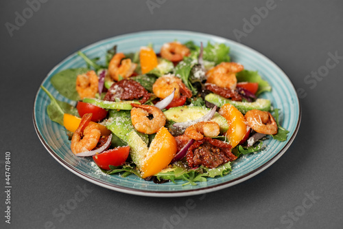 A plate of salad with shrimp, arugula and other vegetables, one plate on a gray table, food for health