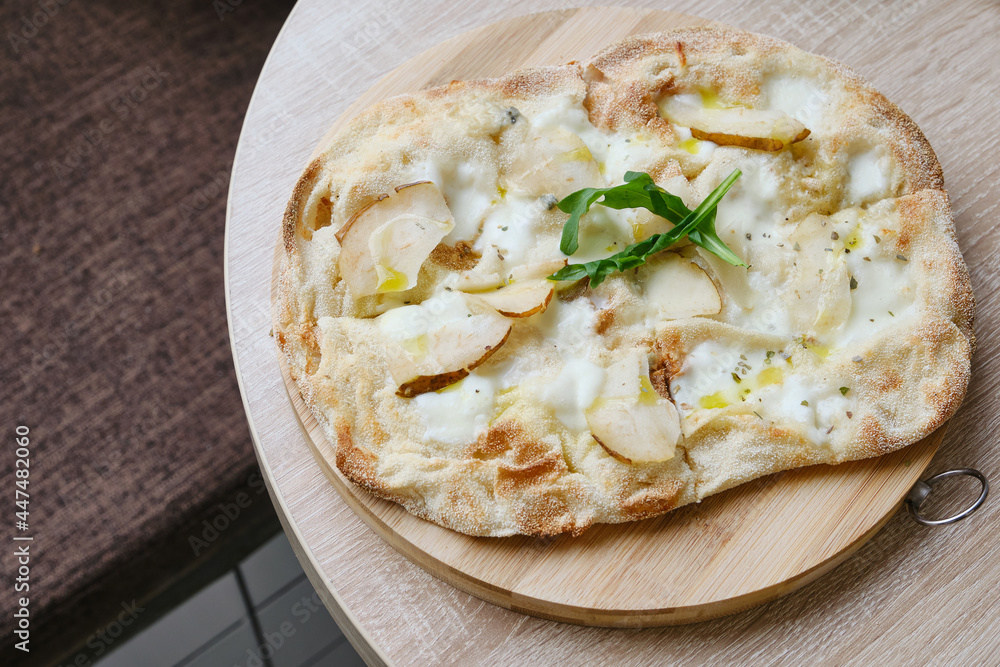 Roman round pizza five or four cheeses with baked pear on a round wooden kitchen pizza board. Delicious fresh Italian pizza on a round wooden table. Selective focus Roman round pizza five or four cheeses with baked pear on a round wooden kitchen pizza board. Delicious fresh Italian pizza on a round wooden table. Selective focus
