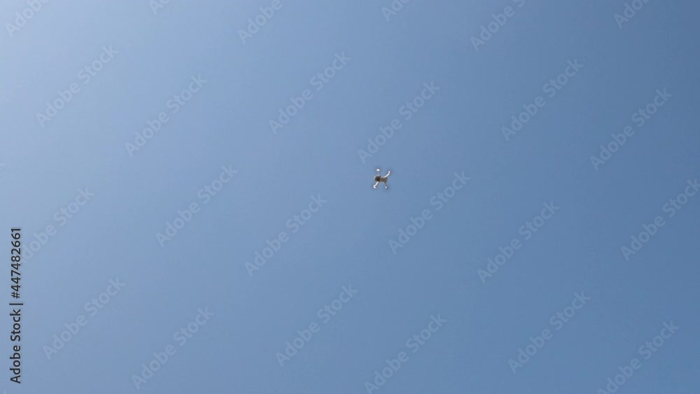 White drone with digital camera flies on blue sky background. White drone with digital camera flies on blue sky background.