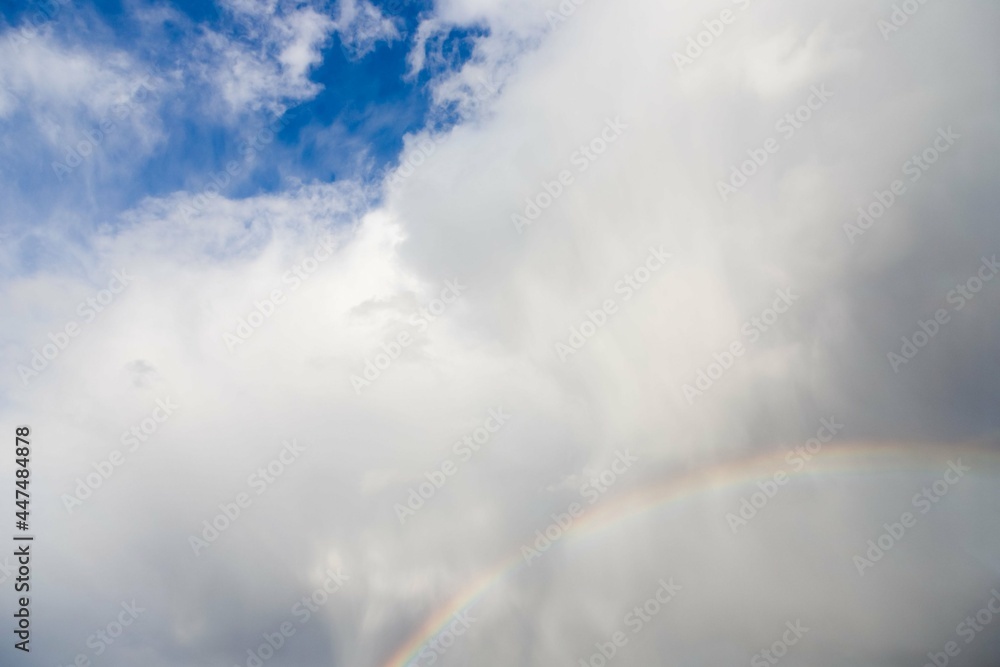 Rainbow and rainy gray white blue sky with fluffy clouds