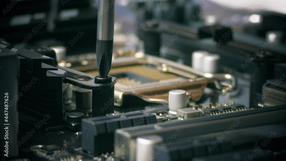 Computer assembly. A close-up of a screwdriver screwing a black fixing bolt into the mount of a cooler of a desktop motherboard. Computer assembly. A close-up of a screwdriver screwing a black fixing bolt into the mount of a cooler of a desktop motherboard.