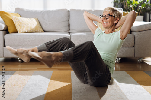 Happy senior woman doing sit-ups with hands behind her head in the living room photo