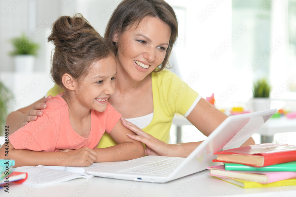 Smiling mother and daughter doing homework with help of laptop together Smiling mother and daughter doing homework with help of laptop together