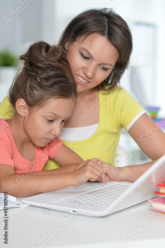  Smiling mother and daughter doing homework with help of laptop together