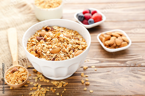 Tasty granola in bowl and spoon with fruits and almonds on brown wooden background