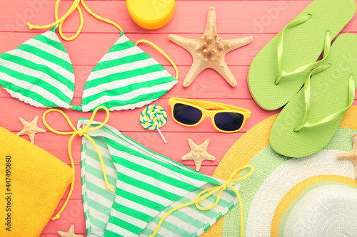 Swimsuit with flip flops, sunglasses, straw hat, lollipop and starfishes on pink background