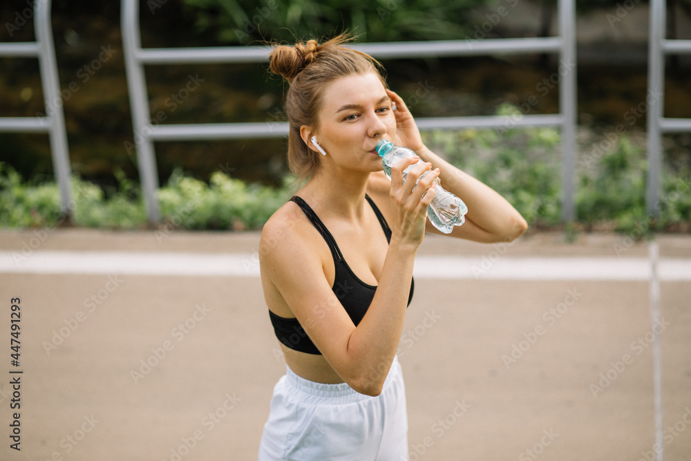 Beautiful young sportswoman woman drinks water from a plastic bottle, quenches her thirst while doing sports Beautiful young sportswoman woman drinks water from a plastic bottle, quenches her thirst while doing sports