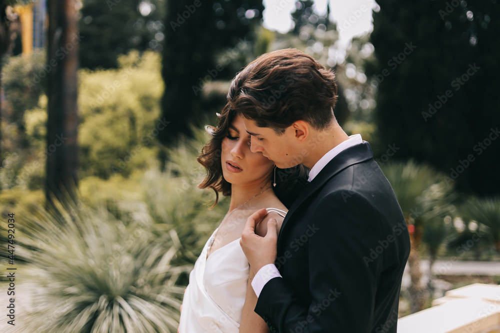 The concept of a wedding in nature. A love story of a man and a woman in wedding dresses walking among plants and palm trees in an old green park outdoors, a selective focus The concept of a wedding in nature. A love story of a man and a woman in wedding dresses walking among plants and palm trees in an old green park outdoors, a selective focus