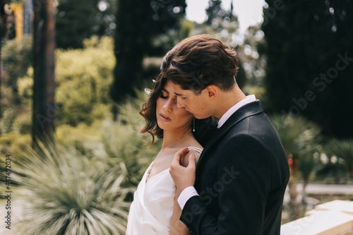 The concept of a wedding in nature. A love story of a man and a woman in wedding dresses walking among plants and palm trees in an old green park outdoors, a selective focus