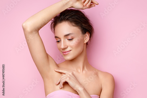 Young woman holding her arm up and showing clean underarm. Photo of smiling woman with smooth skin after epilation on pink background. Beauty concept photo