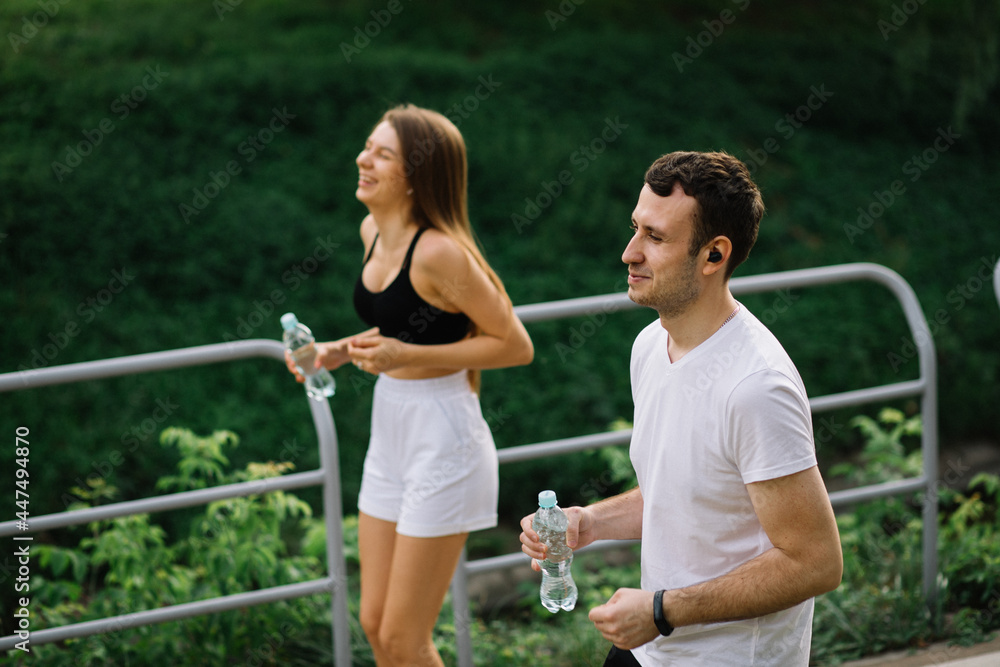 Young couple running in city park with botle of water in hands, joint sports, cheerfulness, city lifestyle Young couple running in city park with botle of water in hands, joint sports, cheerfulness, city lifestyle