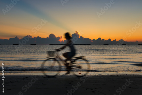 Silhouette with blurred effect of woman by bicycle at the beach at dawn