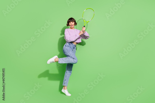 Full length body size view of attractive cheerful girl playing tennis having fun isolated over bright green color background © deagreez