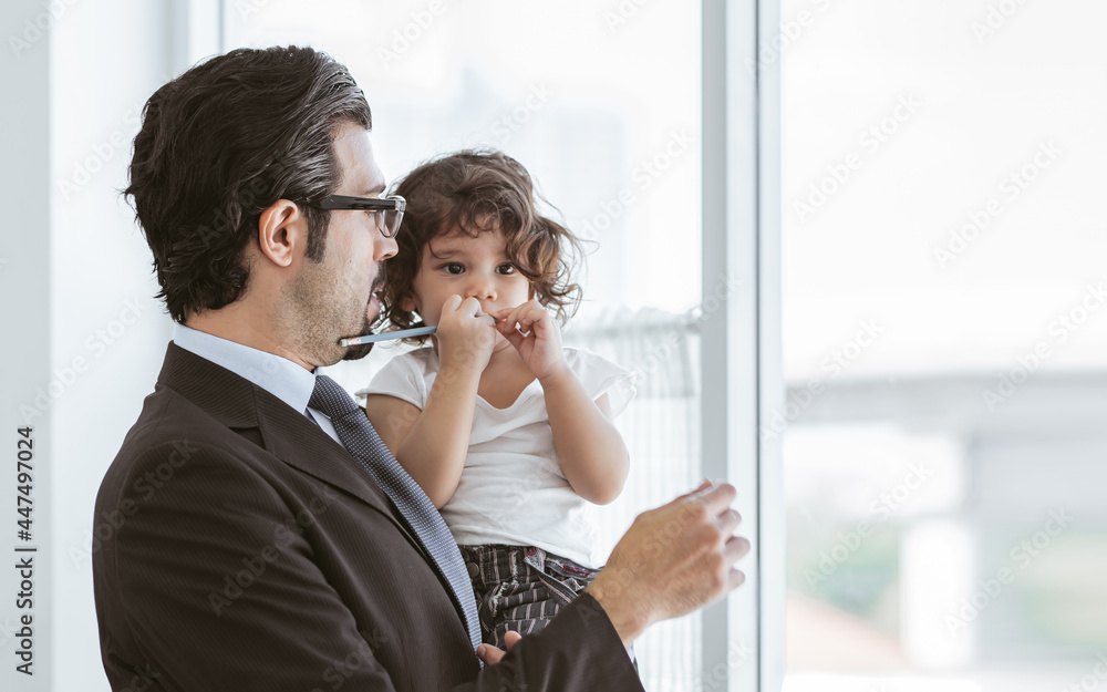 Caucasian beard handsome businessman wearing formal suit for work, carrying and hugging cute little daughter and standing beside window before going to work in morning. Family Concept.