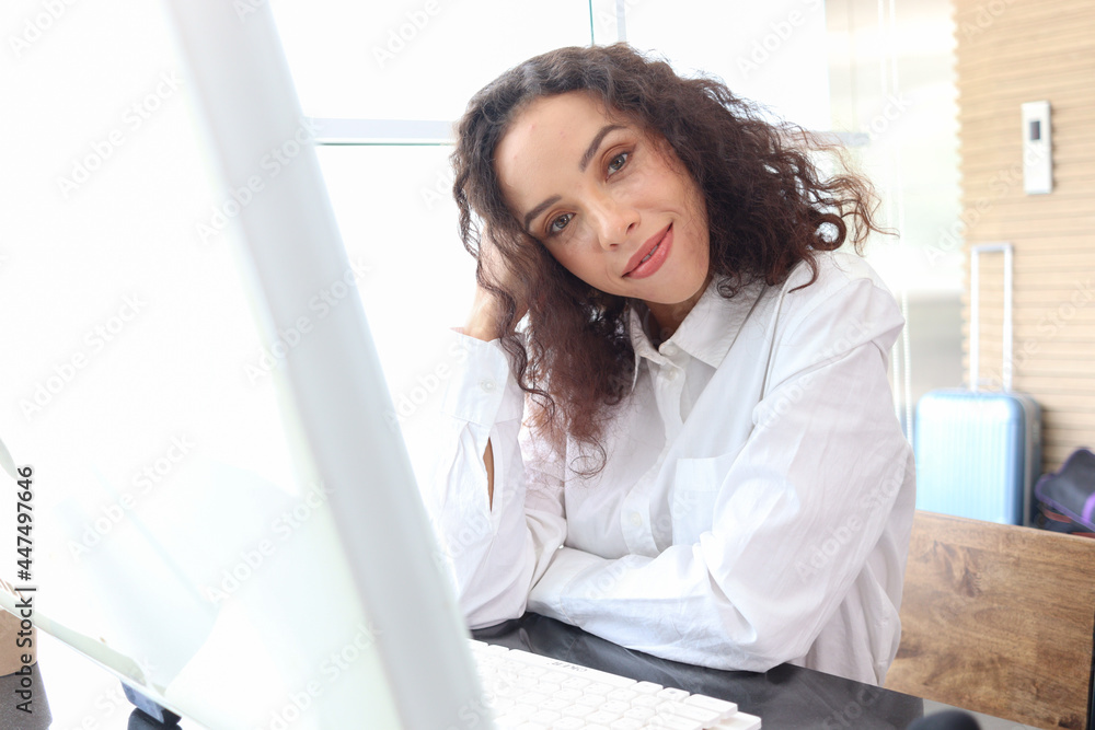 Portrait of happy smiling young beautiful woman with curly hair using desktop computer, female officer staff in casual white shirt sitting at working desk at office workplace. Portrait of happy smiling young beautiful woman with curly hair using desktop computer, female officer staff in casual white shirt sitting at working desk at office workplace.