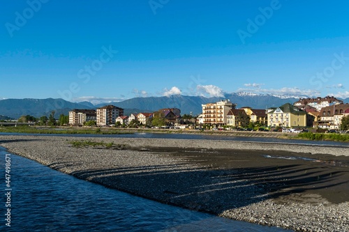 Residential buildings in federal territory of Sirius against backdrop of snow-capped peaks. Caucasus mountains. Imeretinskaya lowland. In foreground is Mzymta.Adler. Sochi, Russia - May 18, 2021 photo