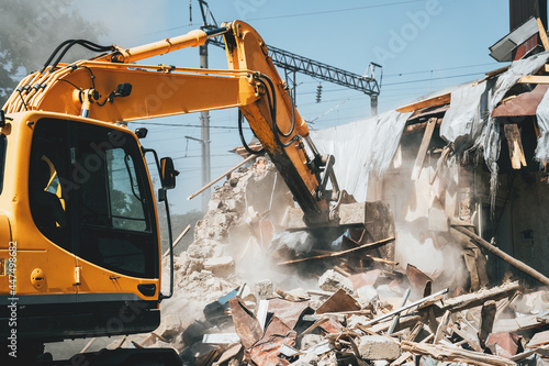 Destruction of old house by excavator. Bucket of excavator breaks concrete structure.