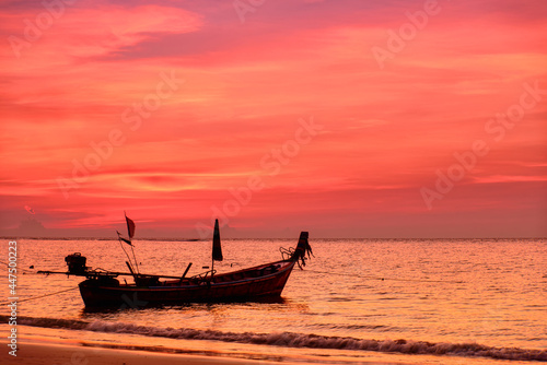 Silhouette of fishing boat on sea beach with sunset background.