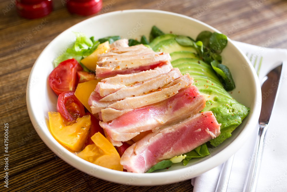 Bowl with tuna, avocado and tomatoes on a wooden table