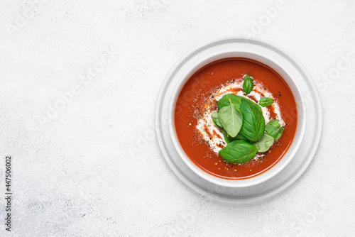 Tomato soup with strachatella cheese and basil. Bowl of fresh vegetable soup on white stone background