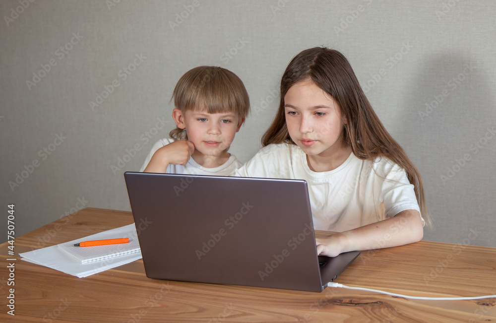 a boy and a girl are sitting at a table and looking at a laptop. The concept of a lesson, training, communication via the Internet a boy and a girl are sitting at a table and looking at a laptop. The concept of a lesson, training, communication via the Internet