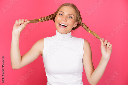 Portrait of cute smiling and fool around woman holding long hair pigtails on red background.