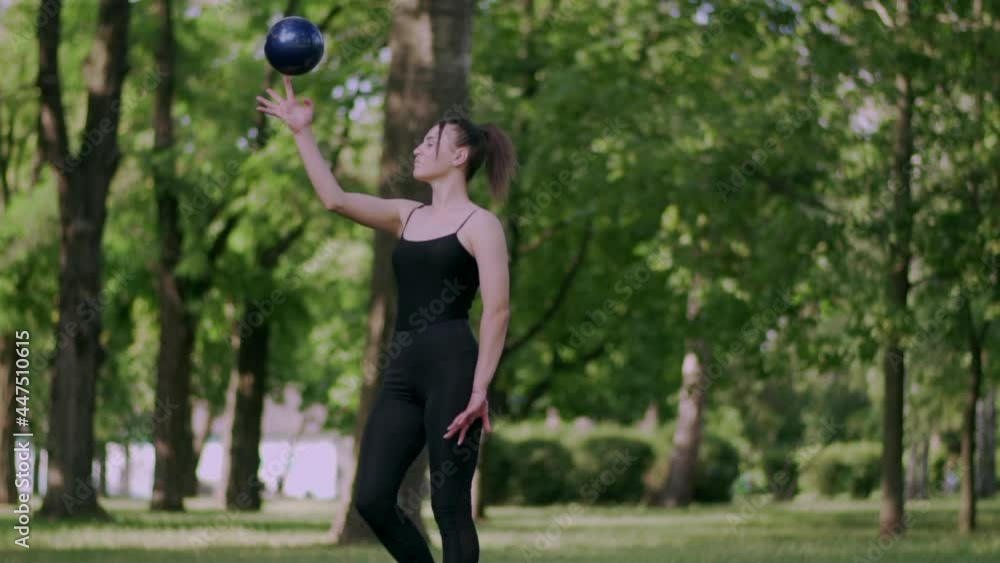 Young woman gymnast performs an exercise with ball in park on sunny day. Slow motion. Medium shot. Young woman gymnast performs an exercise with ball in park on sunny day. Slow motion. Medium shot.