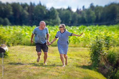 Fototapeta Naklejka Na Ścianę i Meble -  happy middle-aged couple holding hands running in the garden, the concept of a happy relationship