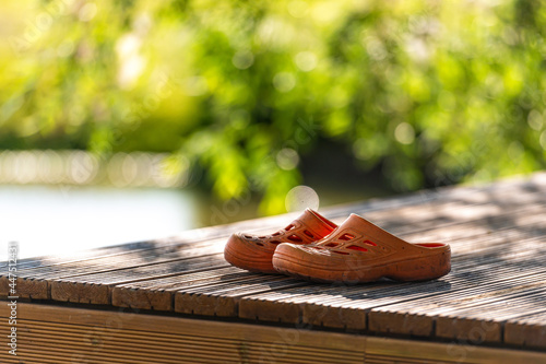 a pair of orange rubber clogs on the pier by the lake, close-up