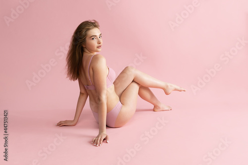 Young beautiful adorable girl in nude color lingerie posing isolated over pink studio background. Natural beauty, spa, cosmetics, fitness and aesthetic cosmetology concept.
