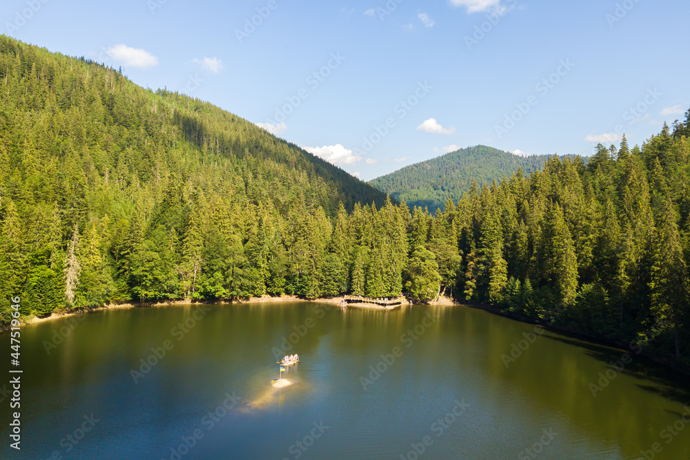 Aerial view of big lake with clear blue water between high mountain hills covered with dense evergreen forest.