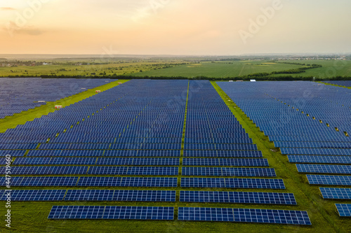 Aerial view of large sustainable electrical power plant with many rows of solar photovoltaic panels for producing clean ecological electric energy in evening. 