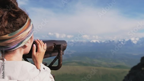 Attractive girl tourist on the observation deck looks at the mountains through binoculars
