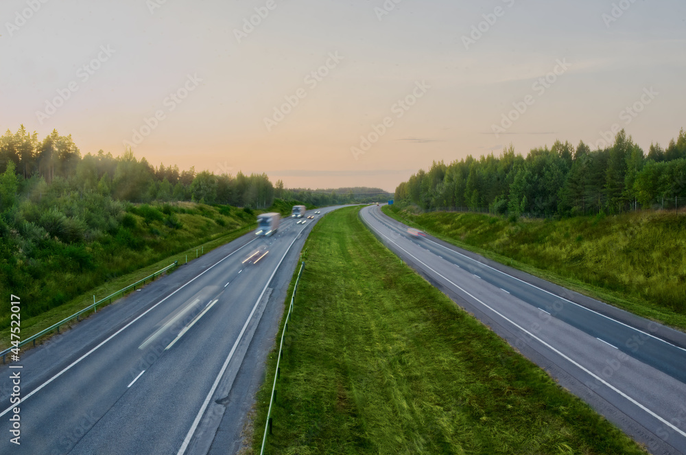 Fast moving cars and trucks at evening in a green highway 