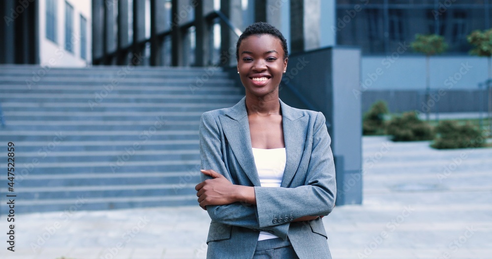 Waist up portrait view of smiling multiracial lady wearing white blouse and suit while standing near business centre and smiling. She is feeling confident Waist up portrait view of smiling multiracial lady wearing white blouse and suit while standing near business centre and smiling. She is feeling confident