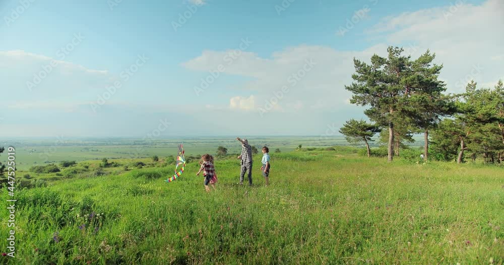 Caucasian cute small teen children jumping at the field with a kite in hands and his grandfather helping to them to launch it on a sunny day. Family concept Caucasian cute small teen children jumping at the field with a kite in hands and his grandfather helping to them to launch it on a sunny day. Family concept